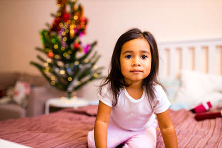 mixed race little cute girl awake in the xmas morning in bedroom and wishing a wish