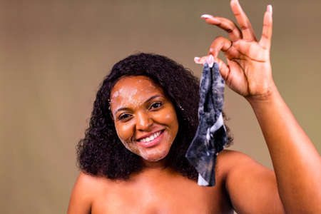 Young woman with bubble sheet mask on her face on brown backgroundの写真素材