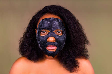 Young woman with bubble sheet mask on her face on brown backgroundの写真素材