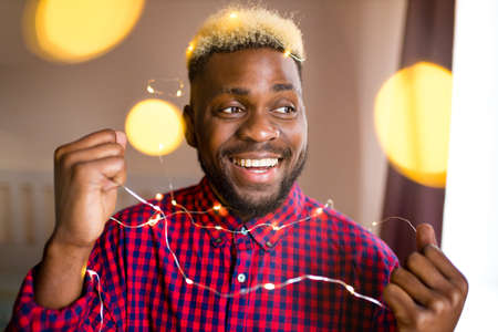 african man making preparations for Christmas party and decorating home with glowing garlandの写真素材