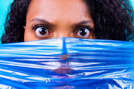 unhappy female with plastic bag on her head against blue wall studio