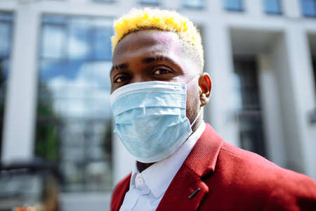mulatto latin businessman in marsala jacket putting on mask prevention air pollution in big sity outdoors office backgroundの写真素材