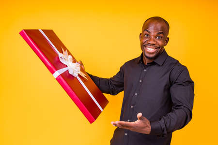 hispanic american man in black t-shirt getting big gift box in studio yellow background