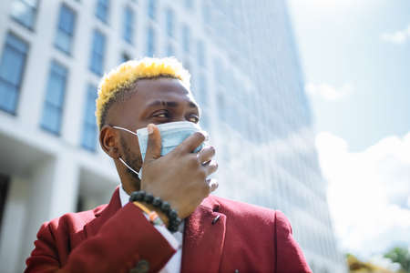 mulatto latin businessman in marsala jacket putting on mask prevention air pollution in big sity outdoors office backgroundの写真素材