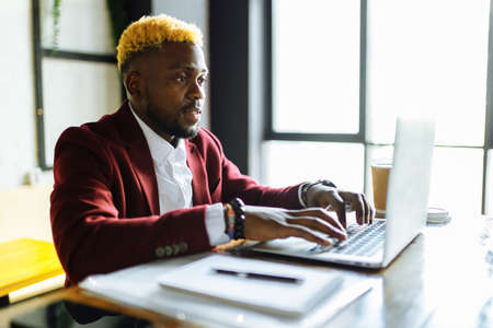Smiling businessman in a marsala jacket working on laptop computer in office