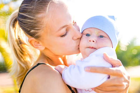 happy blonde woman kissind and feelinf adore to her stroll new born kid in tropics beach park outdoorsの写真素材