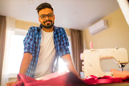 arabian man designer sewing clothes on sewing machine in studio workplace home