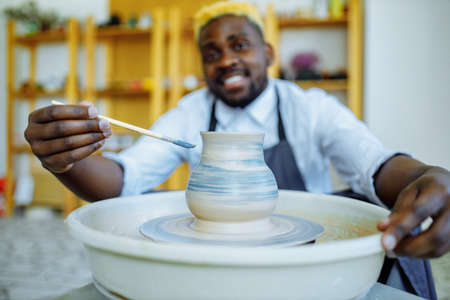 Portrait of positive latin hispanic brazilian man making ceramic pot on pottery wheelの写真素材