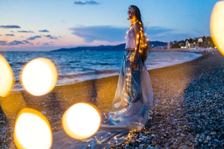 long haired woman in corset with shells on the chest looking languid in twilight near sea beachの写真素材