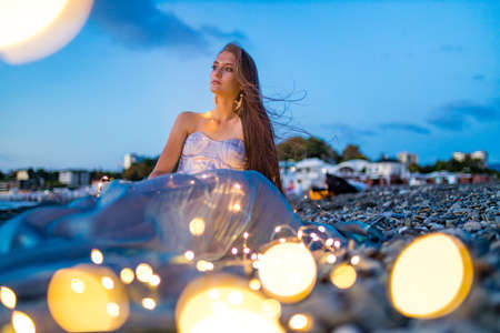 long haired woman in corset with shells on the chest looking languid in twilight near sea beachの写真素材