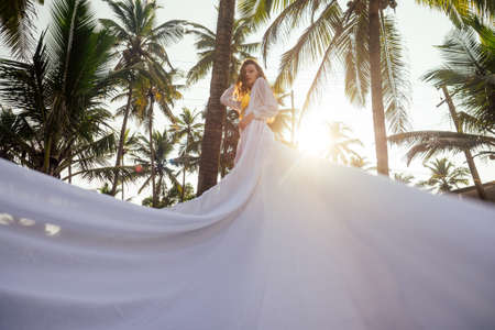 Beautiful brunette woman in white dress with long train on a beach enjoying solitude and freedomの写真素材