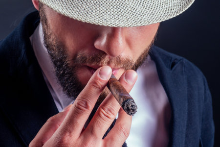 Portrait of an attractive business man with a cigar in black background studioの写真素材