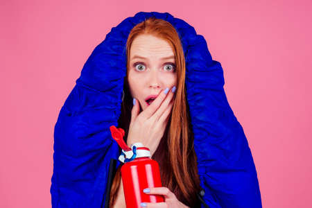 red hair ginger woman holding red bottle and wrapped in in sleeping bagの写真素材