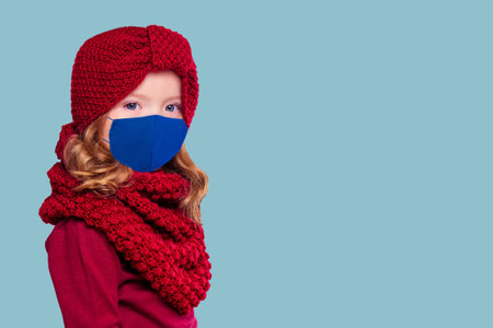 Beautiful little girl in the winter warm hat and scarf and medical mask stylish fashion child look in winter new year timeの写真素材