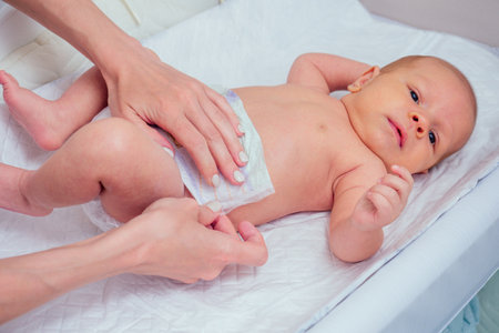 caucasian mother applying baby powder before putting diapers on her four month old baby in bed at homeの写真素材