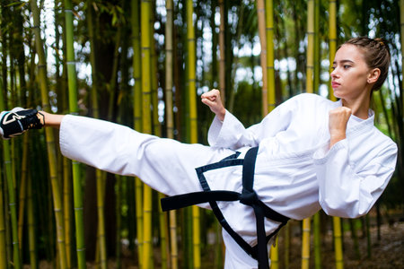 A young woman with a black belt coaches in martial art outdoor bamboo backgroundの写真素材