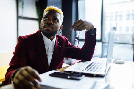 african american person sitting at office typing message note on phone near laptopの写真素材