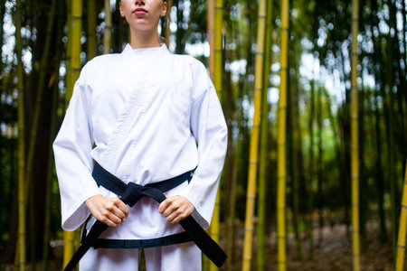A young woman with a black belt coaches in martial art outdoor bamboo backgroundの写真素材