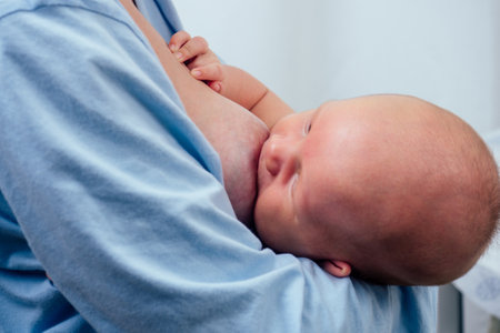blonde mother breastfeeding and hugging baby at cozy apartmentの写真素材