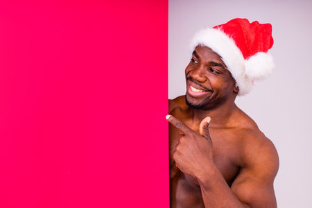 naked nude african american man holding gift box with white ribbon tie bow in red studio backgroundの写真素材