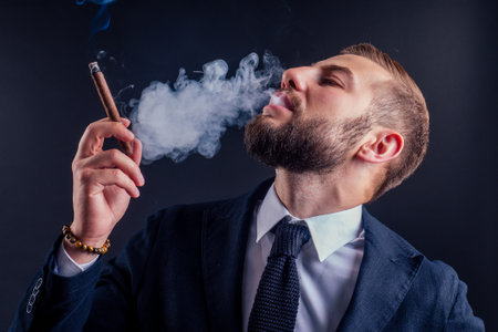 Portrait of an attractive business man with a cigar in black background studioの写真素材