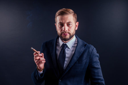 Portrait of an attractive business man with a cigar in black background studioの写真素材