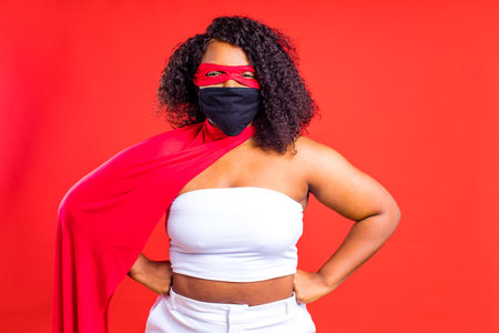 latin hispanic woman in red eye mask and long superhero cloak in studio backgroundの写真素材