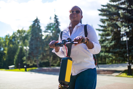 mixed race woman riding an electric scooter in the summer on the streetの写真素材