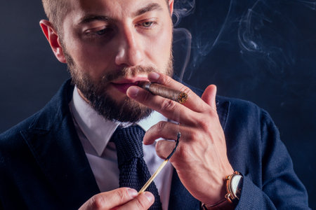 Portrait of an attractive business man with a cigar in black background studioの写真素材