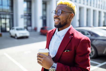 african american man in marsala jacket drinks coffee to go frop paper eco cup outdoor in centre officeの写真素材