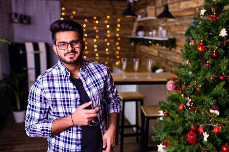 indian man drinking alcohol at studio shot spruce Christmas tree lights garland background