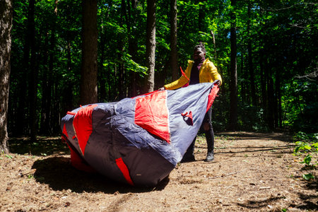 african american in yellow jacker putting on a tent in forest