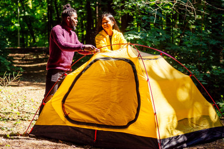 afro american mixed race couple establishing installation a tent and having a rest time outdoorsの写真素材