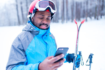 afro american man in blue jacket run ski outdoors in freeze forest holding a phone on handsの写真素材