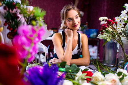 graceful blonde woman in apron selling a flowers in her store ownの写真素材