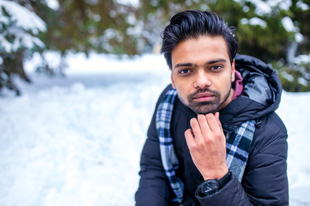 indian man enjoying snowflakes falling from upwards in forest