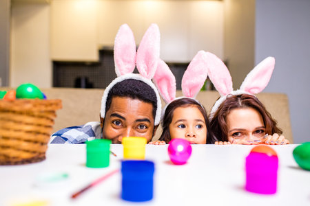 mixed race family painting eggs in cozy kitchenの写真素材