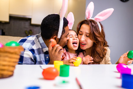 afro american man and caucasian woman ans their cute child painting eggs indoorsの写真素材
