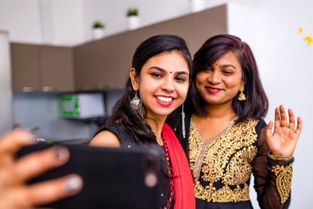 two indian women in saree talk with family by phone video chatting at living room in home