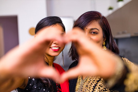 two indian women with bindi on the forehead hugging in living roomの写真素材