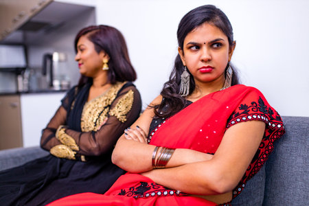 two young indian women in traditional sari and bindi looking in different sides in interior of living roomの写真素材