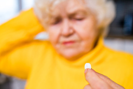 Ill old woman taking a pill from a pill dispenser in her houseの写真素材