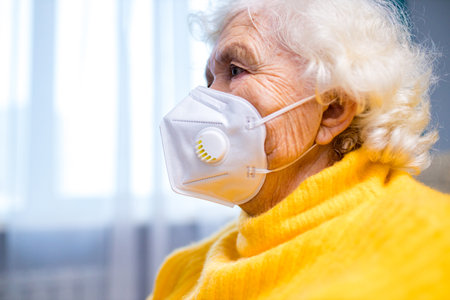 Closeup up portrait of adult woman wearing medical mask and warm yellow sweater indoorsの写真素材