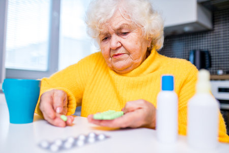 Elderly woman taking pill at home in the kitchenの写真素材