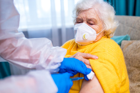 Doctor giving injection to senior woman at her house in living roomの写真素材