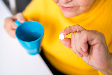 Elderly woman taking pill at home in the kitchenの写真素材