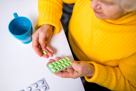 Ill old woman taking a pill from a pill dispenser in her houseの写真素材