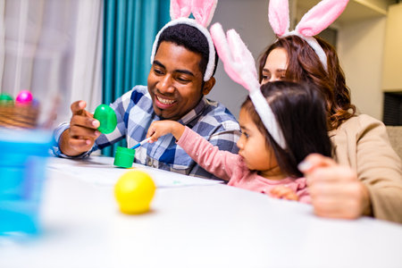 mixed race family painting eggs in cozy kitchenの写真素材