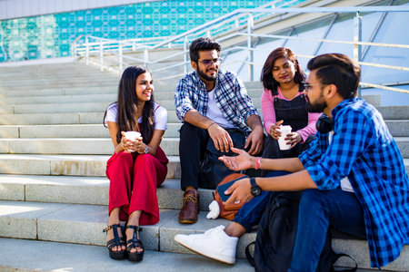 indian friends sitting on stairs outdoors with copybooksの写真素材
