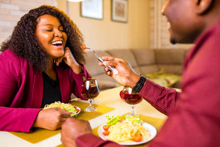 african american couple in love drinking wine from glasses and eating italian pasta in living room...